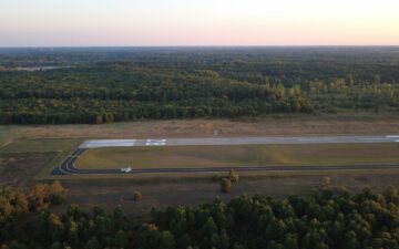 Аэроснимок частного аэродрома, окруженного густым лесом, на закате.