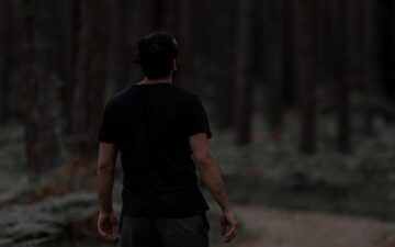Задний вид мужчины, идущего по грязной дорожке в спокойном, густом лесу с размытым фоном.