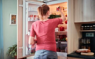 Женщина открывает холодильник, чтобы достать продукты в уютной кухонной обстановке.