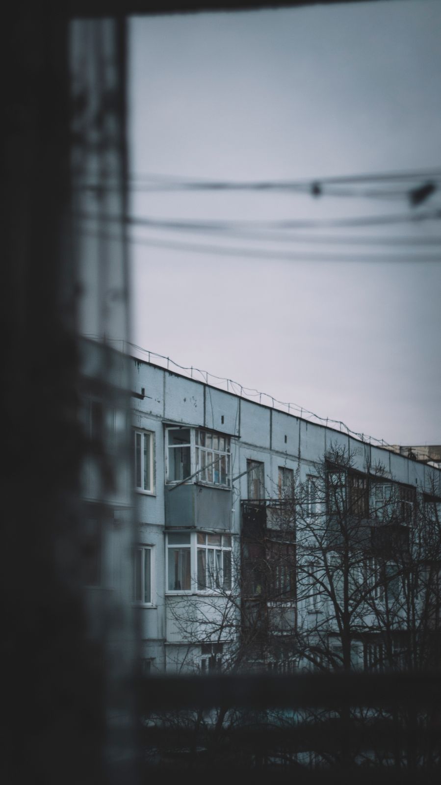 Настроенческий вид на городской жилой блок через окно в облачный день, запечатлевающий созерцательную городскую сцену.