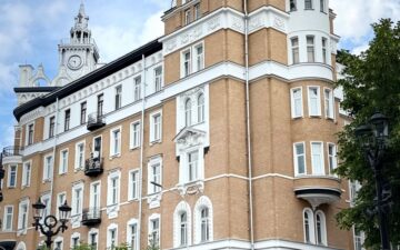 Живописное историческое кирпичное здание с богато украшенными башенками на фоне ярко-голубого неба с облаками.