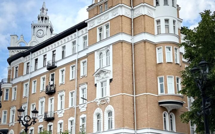 Живописное историческое кирпичное здание с богато украшенными башенками на фоне ярко-голубого неба с облаками.
