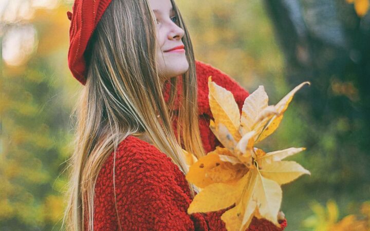 Молодая женщина в красной одежде держит осенние листья на улице в парке.