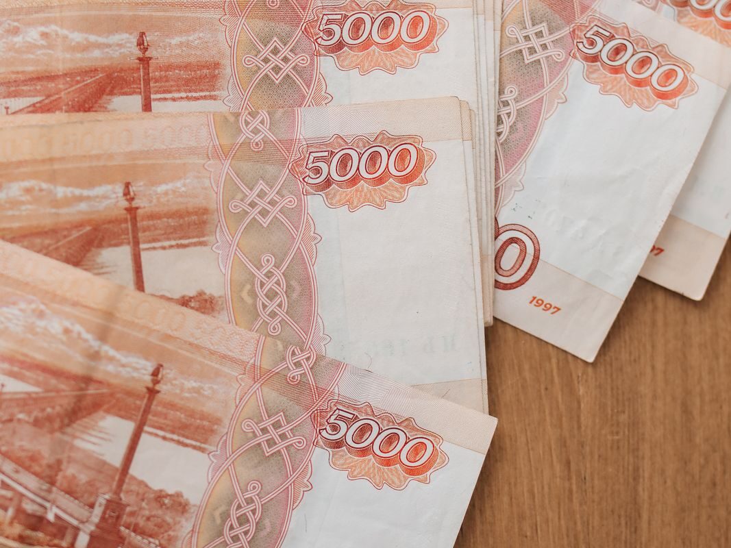Вид сверху на банкноты в 5000 российских рублей, размещенные на деревянной поверхности, отображающие детали валюты.