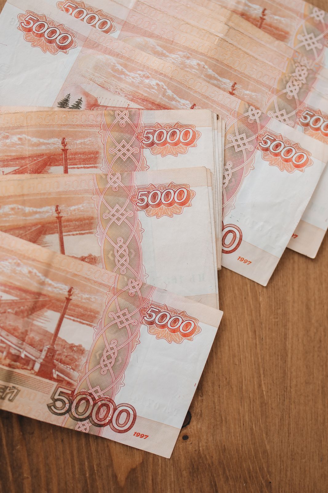 Вид сверху на банкноты в 5000 российских рублей, размещенные на деревянной поверхности, отображающие детали валюты.