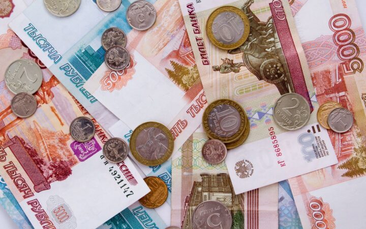 Подробное изображение банкнот русского рубля с различными монетами, разбросанными сверху, демонстрирующее детали валюты.